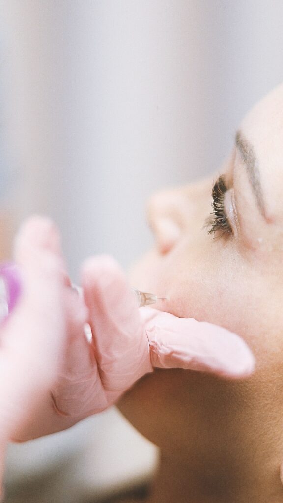 A professional performing a cosmetic injection on a woman's cheek in a clinic.